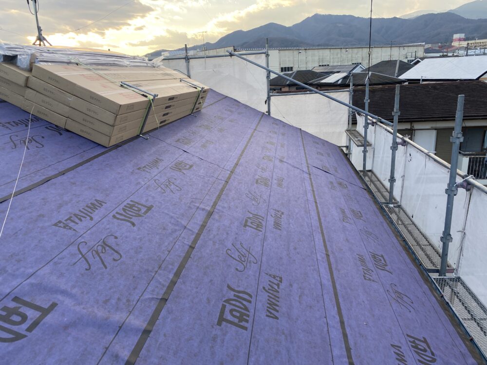 夕暮れ・丹沢を背景に防水シートが張られた屋根・屋根材の箱が積んである